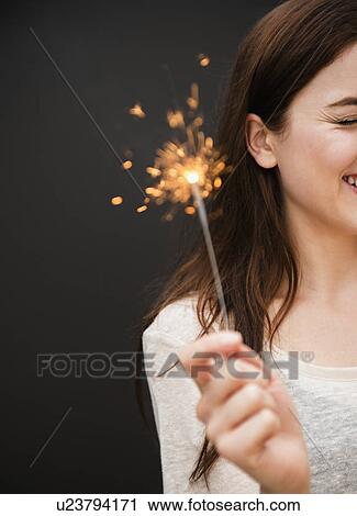 Stock Image - Young woman holding firework. Fotosearch