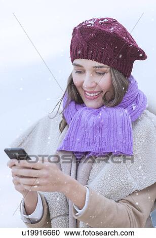 Stock Image - Young woman in wearing warm clothes and using mobile phone. Fotosearch
