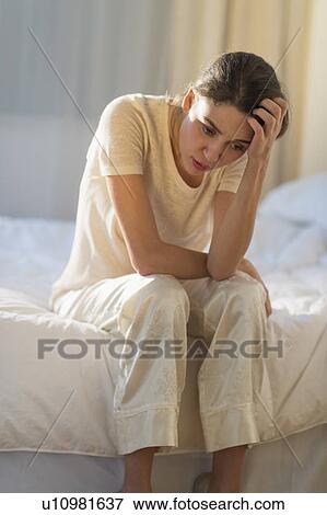 Stock Photo - Young woman sitting on bed with headache. Fotosearch