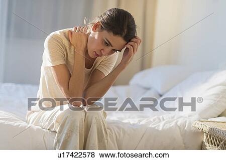 Young woman sitting on bed with headache View Large Photo Image Stock Photo - Young woman sitting on bed with headache. Fotosearch