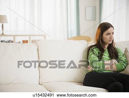 Stock Image - Young woman sitting on couch. Fotosearch