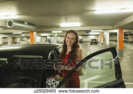 Stock Image - Young woman standing next to open car door. Fotosearch