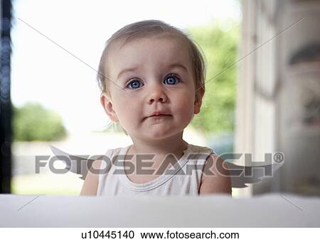 Stock Image - Baby girl wearing fairy wings at table. Fotosearch