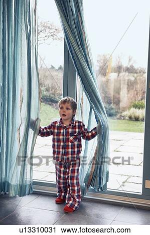 Stock Image - Boy in pajamas playing in curtain. Fotosearch