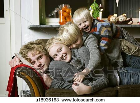 Stock Image - Boys piled together on sofa. Fotosearch