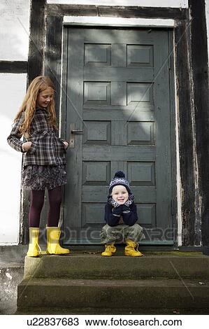 Stock Image - Brother and sister smiling on doorstep. Fotosearch