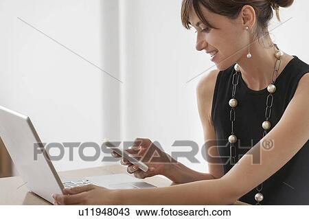 Stock Image - Businesswoman using cell phone at desk. Fotosearch