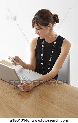 Stock Photograph - Businesswoman using cell phone at desk. Fotosearch