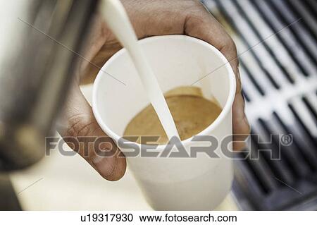 Stock Image - Close up of milk pouring into coffee cup. Fotosearch