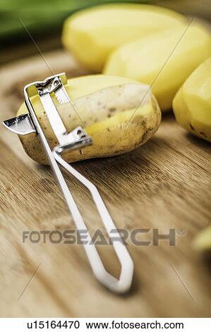 Stock Image - Close up of peeler and potatoes. Fotosearch