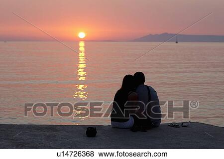 Couple relaxing on pier at sunset View Large Photo Image Stock Photo - Couple relaxing on pier at sunset. Fotosearch