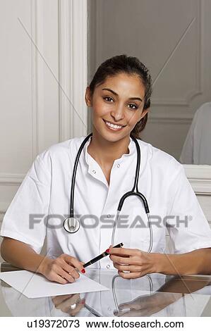 Doctor smiling at desk in office View Large Photo Image Stock Image - Doctor smiling at desk in office. Fotosearch