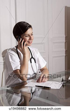 Stock Image - Doctor talking on cell phone in office. Fotosearch