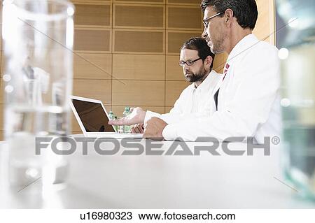 Stock Image - Doctors using laptop at desk. Fotosearch