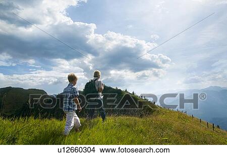 Picture - Father and son hiking on grassy hilltop. Fotosearch