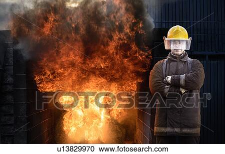 Stock Image - Firefighter standing by blaze. Fotosearch