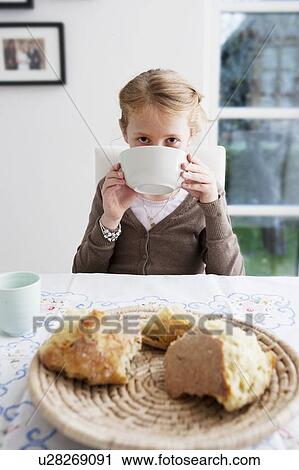 Stock Image - Girl drinking soup from bowl at table. Fotosearch