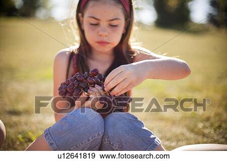 Stock Photo - Girl eating bunch of grapes in field. Fotosearch