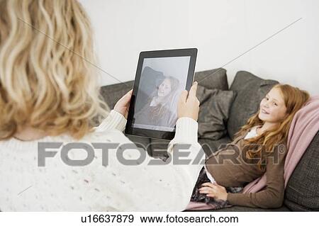 Stock Photo - Girl taking picture of sister on sofa. Fotosearch