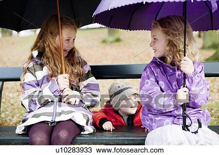 Girls with umbrellas on park bench View Large Photo Image Stock Image - Girls with umbrellas on park bench. Fotosearch
