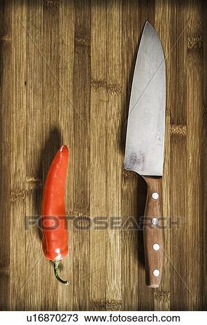 Stock Image - Knife and chili pepper on wooden table. Fotosearch