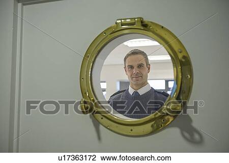Stock Image - Man looking through ships porthole. Fotosearch