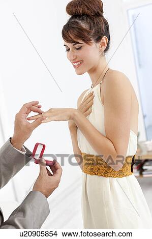 Picture - Man putting engagement ring on fiance. Fotosearch