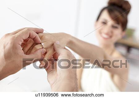 Man putting engagement ring on fiance View Large Photo Image Stock Photograph - Man putting engagement ring on fiance. Fotosearch