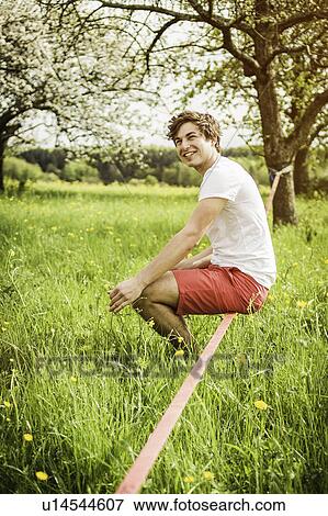 Stock Photo - Man sitting on tightrope in field. Fotosearch