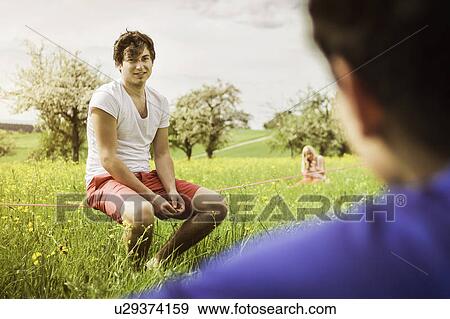 Stock Photo - Man sitting on tightrope in field. Fotosearch
