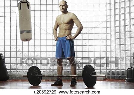 Stock Photo - Man standing with weights in gym. Fotosearch