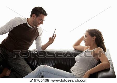 Stock Photo - Man taking picture of girlfriend on sofa. Fotosearch