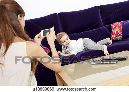 Stock Photo - Mother taking picture of son on sofa. Fotosearch