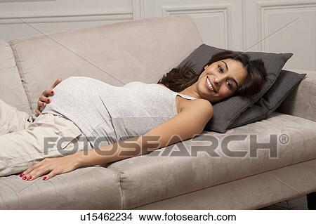 Pregnant woman holding belly on sofa View Large Photo Image Picture - Pregnant woman holding belly on sofa. Fotosearch