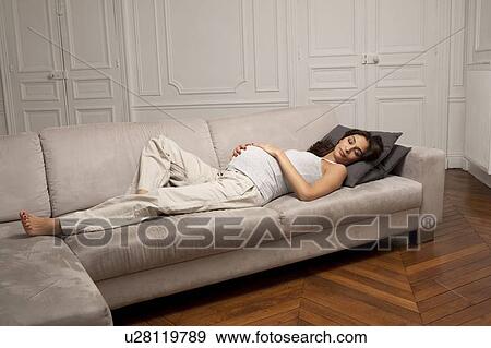 Stock Photo - Pregnant woman holding belly on sofa. Fotosearch