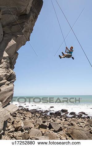 Stock Image - Rock climber abseiling jagged cliff. Fotosearch