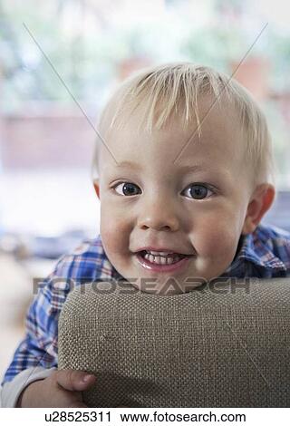 Stock Image - Smiling boy leaning on arm of chair. Fotosearch