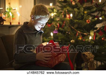 Stock Image - Smiling boy opening Christmas present. Fotosearch