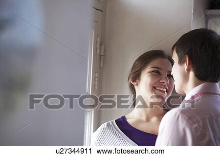 Stock Image - Smiling couple standing by window. Fotosearch