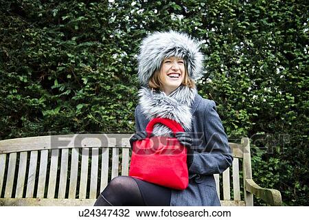 Stock Image - Smiling woman sitting on park bench. Fotosearch