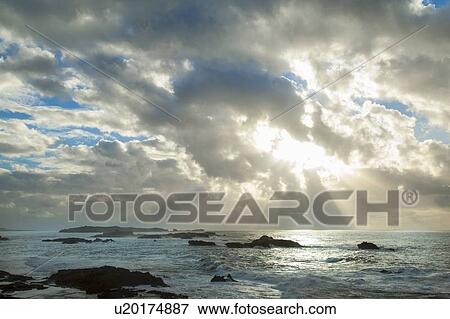 Stock Photo - Sun shining through clouds over beach. Fotosearch