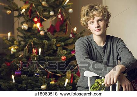 Teenage boy sitting by Christmas tree View Large Photo Image Stock Photo - Teenage boy sitting by Christmas tree. Fotosearch