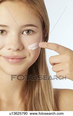 Stock Image - Teenage girl moisturizing her face. Fotosearch