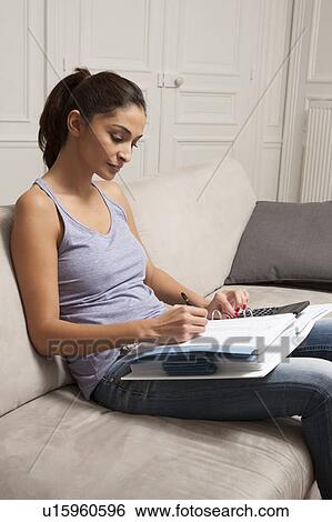 Stock Photograph - Woman doing homework on sofa. Fotosearch