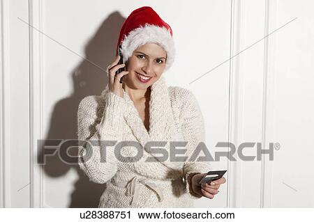 Stock Image - Woman in Santa hat talking on cell phone. Fotosearch