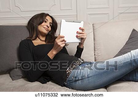 Stock Image - Woman using tablet computer on sofa. Fotosearch