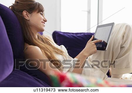 Stock Image - Woman using tablet computer on sofa. Fotosearch