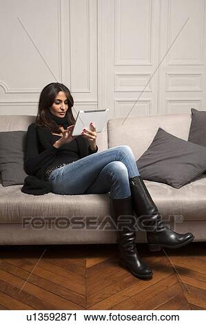 Stock Image - Woman using tablet computer on sofa. Fotosearch