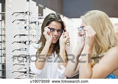 Stock Photo - Women trying on glasses in store. Fotosearch