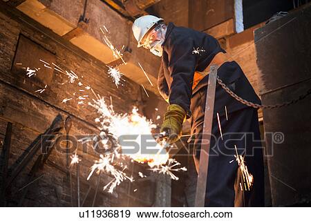 Stock Photo - Worker cleaning mould in metal foundry. Fotosearch